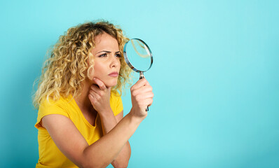 Girl with magnifier lens is distrustful about something. Cyan background