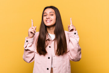 Young Indian woman isolated on yellow background indicates with both fore fingers up showing a...