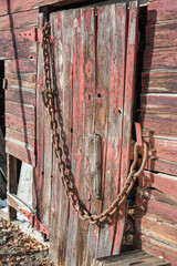 An old abandoned barn door with chain padlock illuminated by sunshine.
