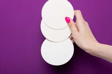 Fototapeta na wymiar Female hand holds a group coasters on a purple background. Hands with pink manicure. Flat lay style