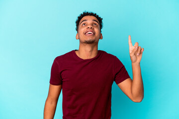 Young african american curly man isolated on blue indicates with both fore fingers up showing a...