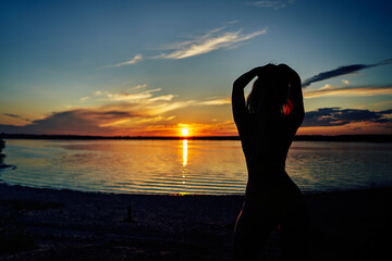 Female silhouette by the water at sunset.