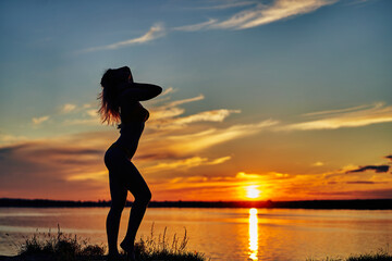 Female silhouette by the water with long hair. Sunset on the paradise beach in the background.