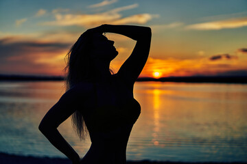 Beautiful silhouette of young woman in sea on sunset background.