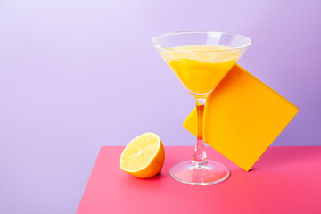 Glass of yellow cocktail with lemon on bright colorful background