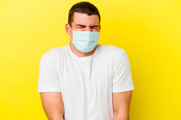 Young caucasian man wearing a protection for coronavirus isolated on yellow background laughs and closes eyes, feels relaxed and happy.