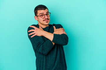 Young caucasian man isolated on blue background hugs, smiling carefree and happy.