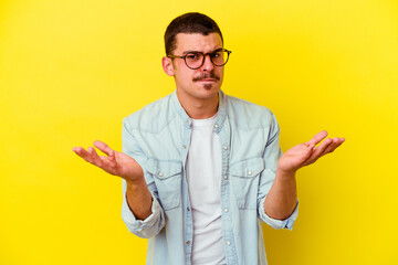 Young caucasian cool man isolated on yellow background doubting and shrugging shoulders in...