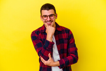 Young caucasian cool man isolated on yellow background smiling happy and confident, touching chin with hand.