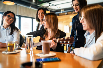 Adult mileninal women playing guitar at cafe or restaurant having fun celebrating - friendship and...