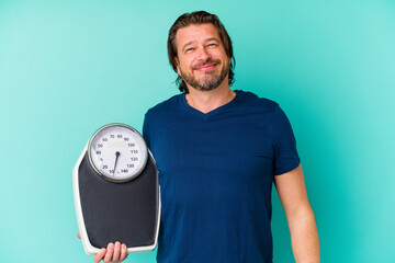 Middle age dutch man holding a scale isolated on blue background happy, smiling and cheerful.