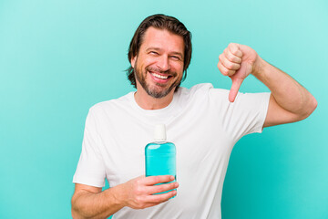 Middle age dutch man sitting holding a mouthwash isolated on blue background showing a dislike gesture, thumbs down. Disagreement concept.