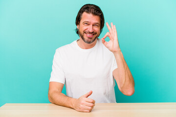 Middle age dutch man sitting isolated on blue background cheerful and confident showing ok gesture.