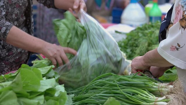 Close up of woman buying fresh green spinach at food market. Variety of green vegetables and herbs on stall at street food market.