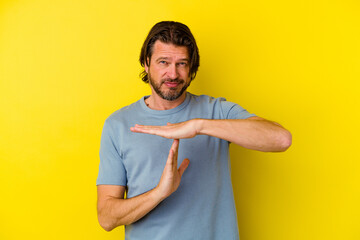 Middle age caucasian man isolated on yellow background showing a timeout gesture.