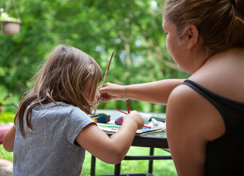 Young Girl and an adult Woman paint Rocks on a Patio Table