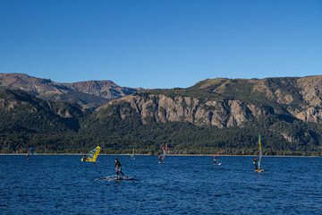 People windsurfing on a blue lake next to huge mountains on a summer evening.