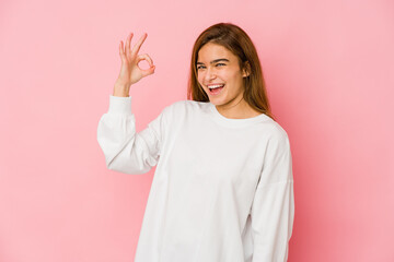 Young skinny caucasian teenager girl winks an eye and holds an okay gesture with hand.