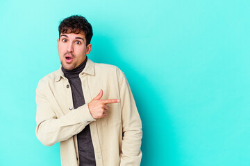 Young caucasian man isolated on blue background smiling and pointing aside, showing something at blank space.