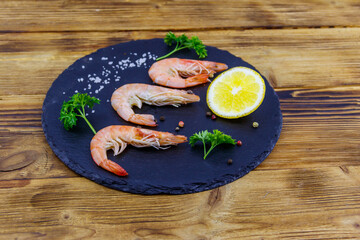 Big raw red prawns with lemon, parsley, salt and pepper on a slate board on wooden table