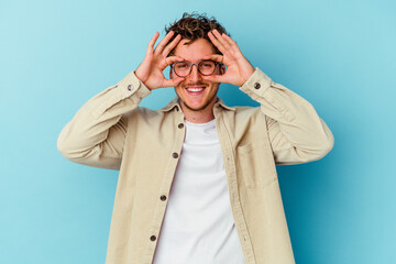 Young caucasian man wearing eyeglasses isolated on blue background excited keeping ok gesture on...