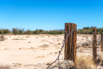 Wooden fence post with rusty barbed wire in a sandy field