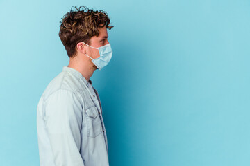Young caucasian man wearing an antiviral mask isolated on blue background gazing left, sideways pose.