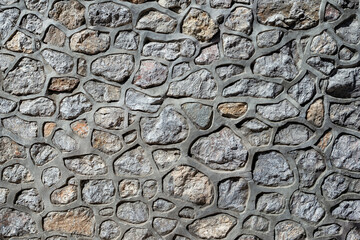 Full screen texture of modern stone masonry of gray limestone cobblestones with wide cement seams
