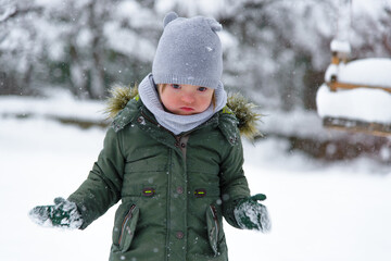 Down syndrome toddler boy in a winter outfit, a warm grey scarf  in a green jacket gloves enjoys...