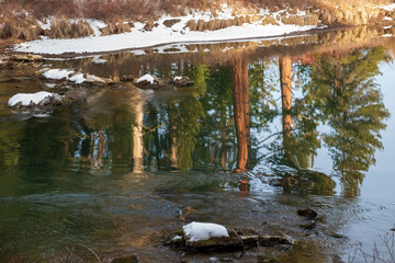 Reflections of a blue sky and trees in a fast-moving river
