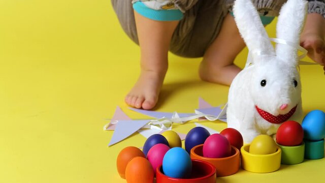 little cheerful boy in bunny grey costume with bunny ears playing with toy rabbit, colorful eggs on trendy ultimate yellow background, slow motion, Happy And Fun Easter Day concept celebrate