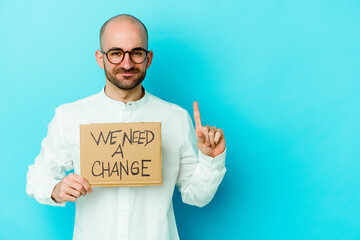 Young caucasian bald man holding a We need a change placard isolated on purple background showing number one with finger.