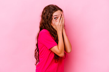 Little caucasian girl isolated on pink background blink through fingers frightened and nervous.