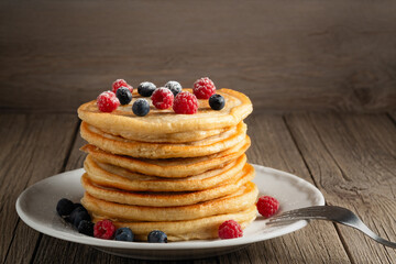 Stack of pancakes with fresh berries on a white plate on the table, copy space