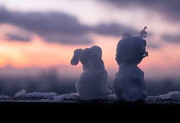 Two snow figurines look out at the evening sky during winter. 