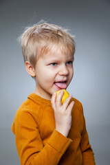 Happy child eating lemon in gray studio