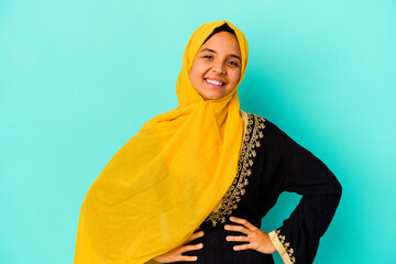 Young muslim woman isolated on blue background confident keeping hands on hips.