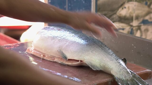 Man cleaning big fresh fish with a knife. Male worker hands processing silver fish.