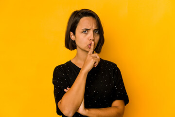 Young hispanic woman isolated on yellow keeping a secret or asking for silence.