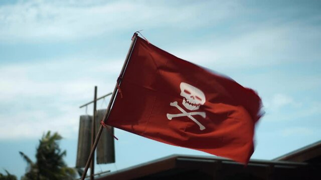 A red pirate flag with a white skull develops in the wind on the street in the tropics