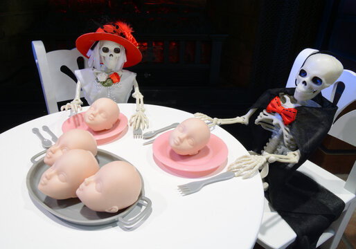 Dressed Up Halloween Skeleton Couple Sitting Down To Dinner Of Plate Of Doll Baby Heads