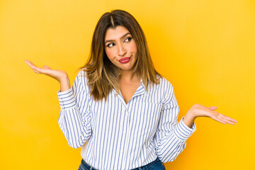 Young indian woman isolated on yellow background confused and doubtful shrugging shoulders to hold a copy space.