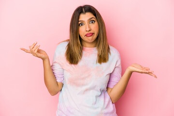 Young indian woman isolated on pink background doubting and shrugging shoulders in questioning...