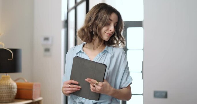 Young business woman going with a digital tablet, sitting on a leather couch at home. Work from home at cozy atmosphere