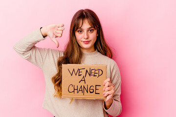 Young caucasian woman holding a We need a change placard isolated showing a dislike gesture, thumbs down. Disagreement concept.