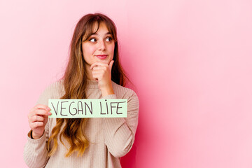 Young caucasian woman holding a vegan life placard isolated looking sideways with doubtful and skeptical expression.