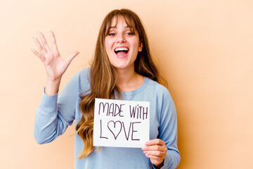 Fototapeta na wymiar Young caucasian woman holding a made with love placard isolated receiving a pleasant surprise, excited and raising hands.