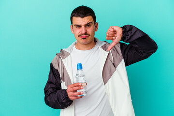 Young sporty caucasian man drinking water isolated on blue background showing a dislike gesture, thumbs down. Disagreement concept.