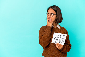 Young hispanic mixed race woman holding a fake news placard relaxed thinking about something looking at a copy space.