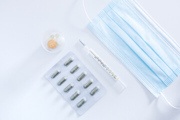Medical objects on white background new surgical face mask, unused thermometer, strip pack of capsule and immune vitamins tablets to protection from spreading of virus pandemic and prevention disease